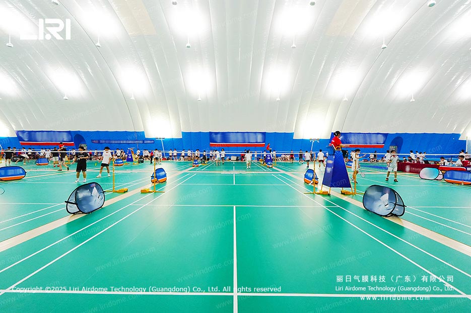 All-weather indoor badminton space with green synthetic courts beneath the curved roof of an air dome