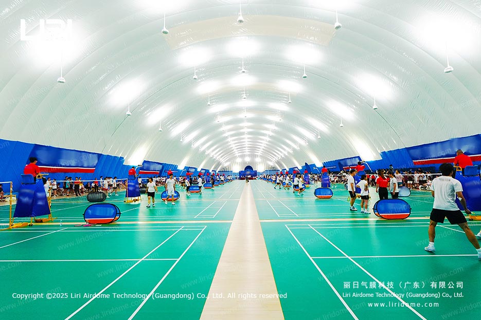 Indoor badminton courts on green synthetic flooring inside an air dome with an arched illuminated ceiling