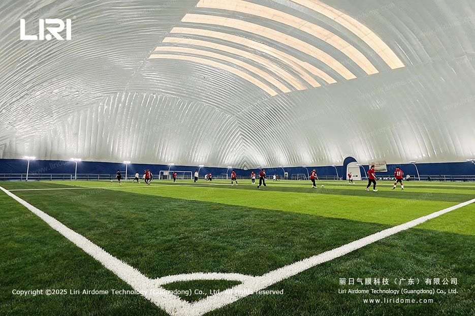 Players training on an indoor football pitch under an air dome
