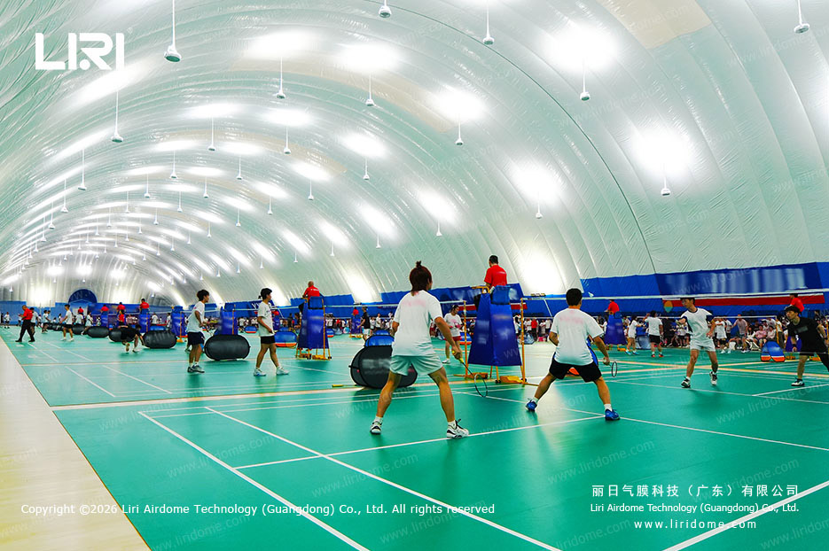 Badminton players competing inside a bright school air dome gymnasium
