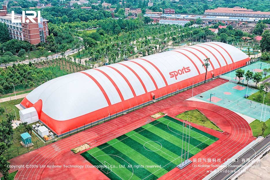 Aerial exterior of a red and white school air dome gymnasium beside a running track